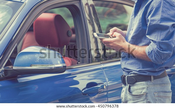 Mobile phone apps for car\
owners concept. Man using smart phone to check status, control  his\
new car