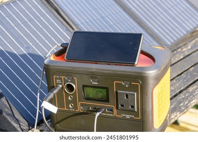 Mobile phone being charged by a solar generator battery pack with solar panels in the sun