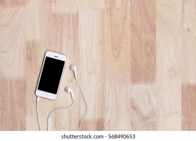 Mobile Phone With Blank Screen And Headphone Smart Phone On Wooden Table Background. Top View With Copy Space