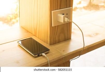 Mobile Phone Charging Plugged On  Wooden Pole In The Coffee Shop With Sunlight In Morning Time.