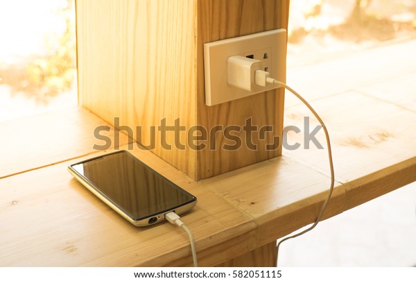Mobile phone charging plugged\
on  wooden pole in the coffee shop with sunlight in morning\
time.