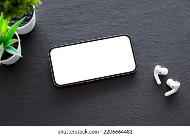 Mobile phone with empty blank screen and earbuds on dark background