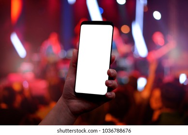 Mobile Phone In Hand With Isolated Screen For Mockup. Music Concert Red Lights And Crowd In Background.