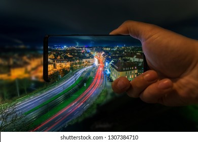 Mobile Phone With Hand At Night In Kassel Germany. From The Cell Phone Comes The Road To The Outside. Long Exposure With Lighttrails. Photoshop Editing