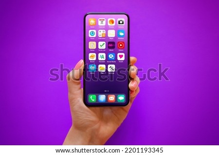 Mobile phone in hand on purple background with sample home screen icons on the screen