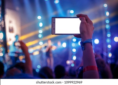 A Mobile Phone In The Hands Of Young People With An Isolated Screen For A Mockup. Live Rock Concert In The Background.