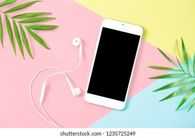 Mobile phone with headphones. Green palm tree leaves. Minimal flat lay background. 