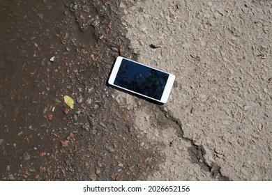 Mobile phone lying on pavement in puddle