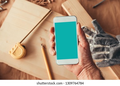 Mobile Phone Mock Up Screen, Male Hand Holding Smartphone With Blank Display As Copy Space In Woodwork Carpentry Workshop