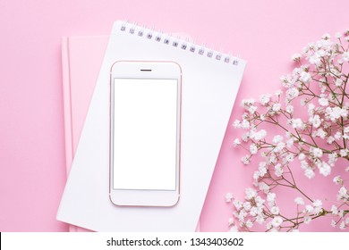 Mobile Phone Mock Up And White Flowers On Pink Pastel Table Top View In Flat Lay Style. Woman Working Desk.Spring Colour