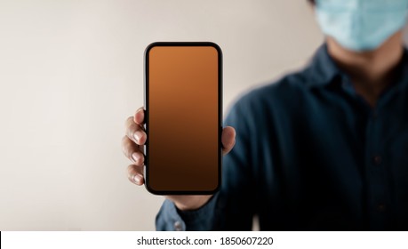 Mobile Phone Mockup Image. Display Screen Is Blank. Person With A Surgical Mask On Face Holding A Smartphone Towards The Camera. Front View