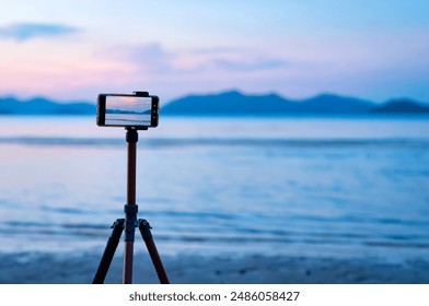 A mobile phone mounted on a tripod photographing sea with twilight sky and cloud, focus picture on screen. Smartphone on tripod taking picture and video of sunset sea coastal landscape, copy space. - Powered by Shutterstock