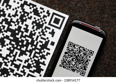 A mobile phone next to a QR code printed on paper