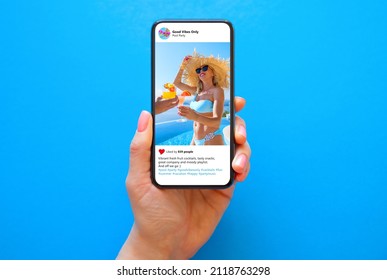 Mobile phone on blue background with shared photo on sample social media app - Shutterstock ID 2118763298