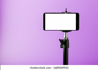 Mobile phone on a tripod with a clear white display for images and text, pink isolated background.