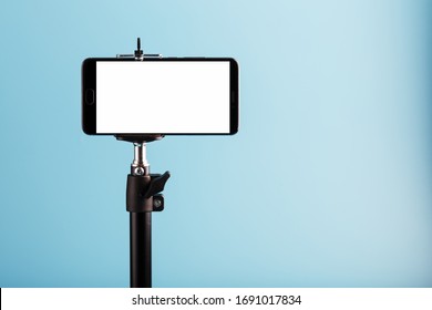 Mobile phone on a tripod with a clear white display for image and text, blue isolated background.