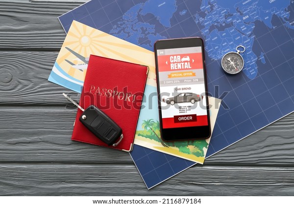 Mobile phone with open car rent app,\
passport, compass and map on dark wooden\
background