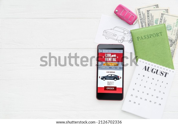 Mobile phone with\
open car rent app, drawn auto, key, passport and calendar on white\
wooden background