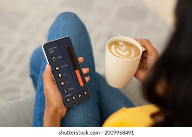 Mobile phone with smart home app, gadgets, house comfort, rest and relax. Young african american woman drinking cappuccino from cup and controlling climate and temperature remotely, double exposure