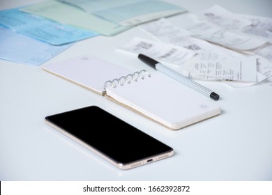 Mobile Phone Or Smartphone With Blank Note Book, A Black Pen, Utility Bills Or Pay Slips And Bank Deposit Account Booklets On White Table Blurred Background