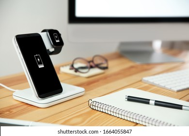 Mobile phone and smartwatch with wireless charger on wooden table. Modern workplace accessory