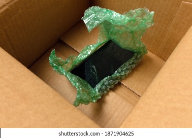 The Mobile Phone Is Wrapped In Bubble Wrap At The Bottom Of A Cardboard Box. Postal Insurance Concept