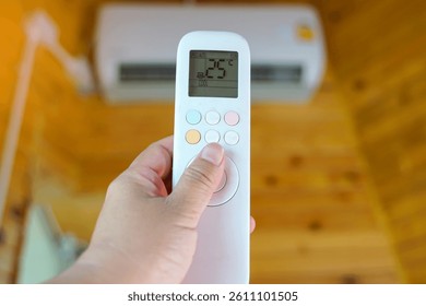 Mobile remote control adjusts the temperature of the air conditioner in the house to 25 degrees Celsius to save electricity. Soft and selective focus.                                