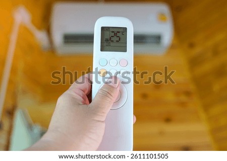 Mobile remote control adjusts the temperature of the air conditioner in the house to 25 degrees Celsius to save electricity. Soft and selective focus.                                