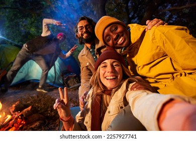 Mobile selfie of Multiracial smiling friends in the forest camping. Young adults with traveling spirit spending time in the countryside at night. Group of happy cheerful colleagues outdoors. - Powered by Shutterstock