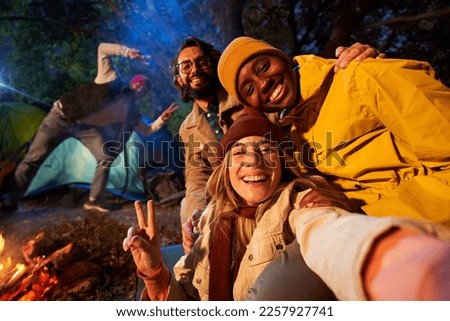 Mobile selfie of Multiracial smiling friends in the forest camping. Young adults with traveling spirit spending time in the countryside at night. Group of happy cheerful colleagues outdoors.