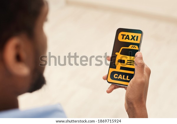 Mobile Service. Over the shoulder view of\
unrecognizable african american guy using modern application,\
ordering a taxi, holding smartphone, calling a cab, black and\
yellow screen app\
interface