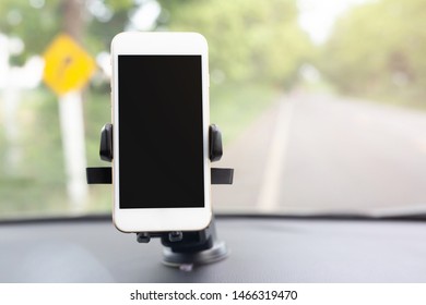 Mobile Smart Phone With Black Screen In Car Console Holder Stick Front. Insert Map Gps Navigation On The In The Background Of The Dashboard. Empty Screen For Text. Copy Space. Car Interior Details.