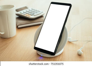 Mobile Smartphone Is Placed On A Wireless Fast Charger. Blank Screen With Clipping Path On Screen For Your Advertising.