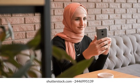 Mobile using. Video call. Happy woman in hijab speaking to friend on cellphone internet conversation checking social network at cozy coffee shop. - Powered by Shutterstock