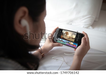 Mobile video editng application concept.Female holding mobile phone and wearing ear phone