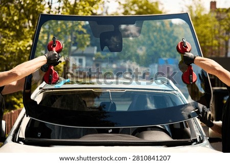 Mobile windshield installation nears completion as technicians carry the new auto glass with vacuum lifters towards the vehicle.
