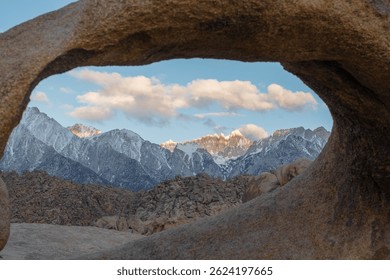 Mobius Arch frames a snowy mountain range in early morning light, with soft golden tones hitting the granite surface, captured May 27, 2019