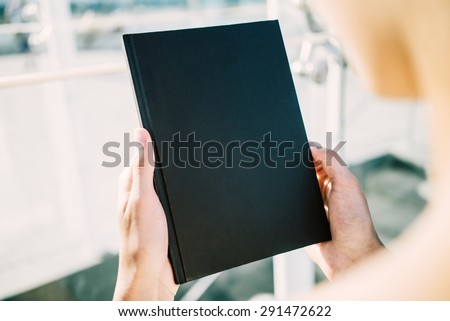 Mock up of black book holding young woman`s  hands
