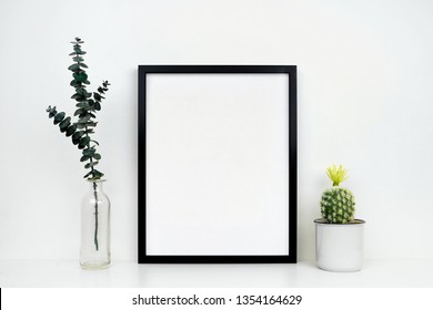 Mock Up Black Frame With Cactus And Branches On A Shelf Or Desk. White Shelf And Wall. Portrait Frame Orientation.