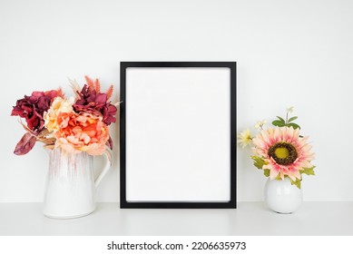 Mock Up Black Picture Frame With Pink Hue Autumn Flowers On A Wood Shelf Against A White Wall. Fall Concept. Copy Space.