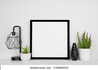 Mock up black square frame with home decor and potted plants. White shelf and wall. Copy space. - Shutterstock ID 1706820292