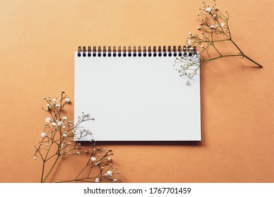 Mock up of blank notepad on ginger background with gypsophila flowers. Top view, flat lay
