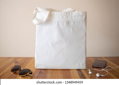 Mock Up Design Bag. Blank White Tote Bag Canvas Fabric With Sunglasses, Smartphone And Headphone On Wooden Table. Eco Or Reusable Shopping Bag. No Plastic Bag And Ecology Concept.
