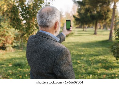 Mock Up Of Elderly Man Using Phone Outside. Green Screen. Back View Of Man Holding Phone At Harm's Length