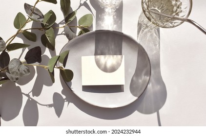 Mock Up Empty Blank Invitation Card, Ceramic Plate Cocktail Glass And Eucalyptus Leaves On Sunlit Background. Summer Mockup Table Setting  For Wedding, Business Or Menu. Harsh Shadows