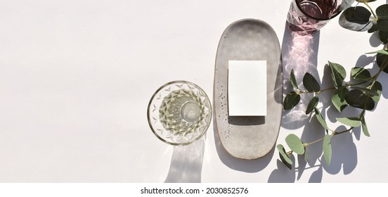 Mock Up Empty Blank Invitation Card, Ceramic Plate Cocktail Glass And Eucalyptus Leaves On Sunlit Background. Summer Mockup Table Setting  For Wedding, Business Or Menu. Long Shadows