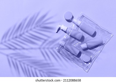 Mock up flatlay with travel size cosmetic bottles in bag on lilac background. Palm leaves shadows. Minimalist bodycare products for vacation or journey. Trendy 2022 color