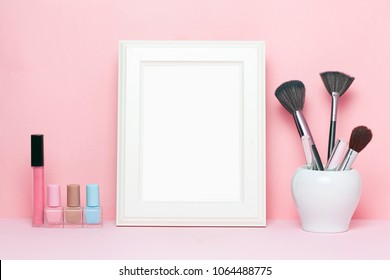 Mock up frame and nail polishes with make up brushes and accessorises women's table with pink background.