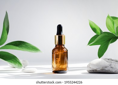 Mock up glass dropper bottle on white gray background with hard shadows, with leaves and stones. Hard shadows. Cosmetic pipette on a white background.