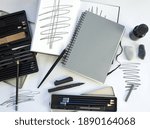 Mock up of gray spiral notebook  for sketch, artwork or logo design. Desk work in white with sketchbooks, pencil, pencil box, pens, ink, quill and other drawing utensils. Blank template.